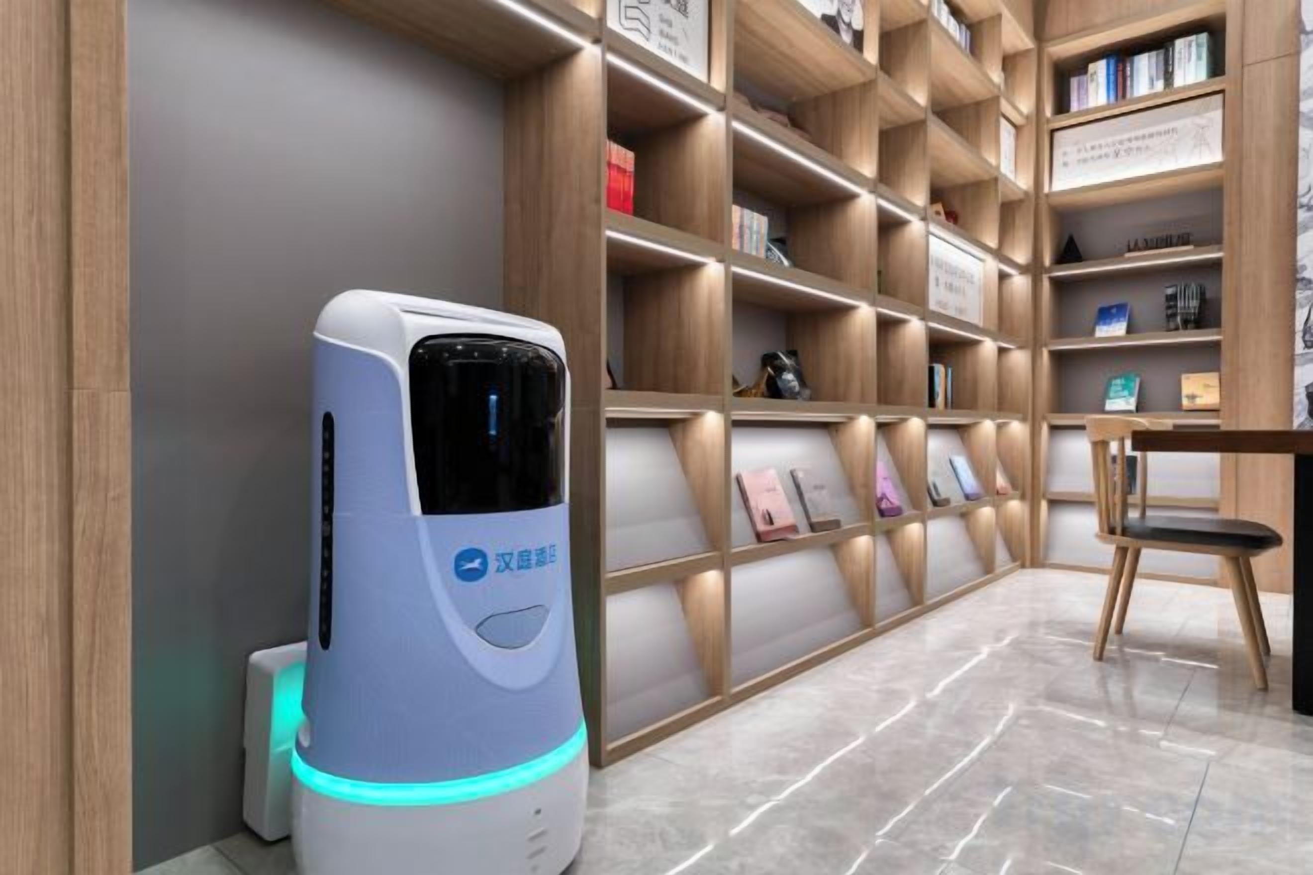 A self-service kiosk with a blue light, a wooden bookshelf with various items, and a chair.