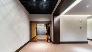Un couloir d’hôtel moderne, doté d’un sol recouvert de moquette, d’une colonne en bois et d’un plafond orné d’un motif géométrique.