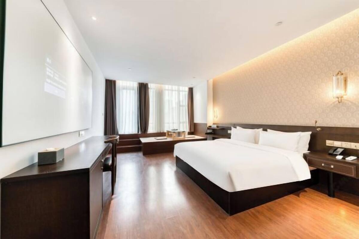 A modern hotel room with a large bed, a desk, a chair, and a TV screen.