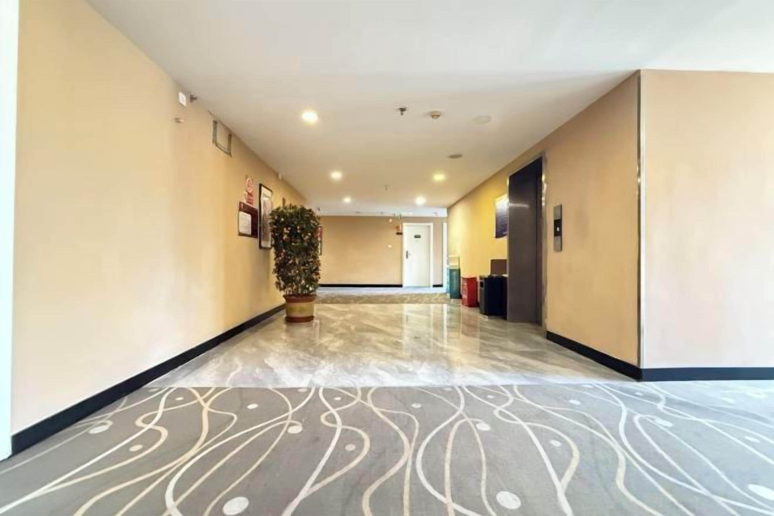 Un pasillo de hotel con piso estampado, una planta en maceta y una puerta al final.