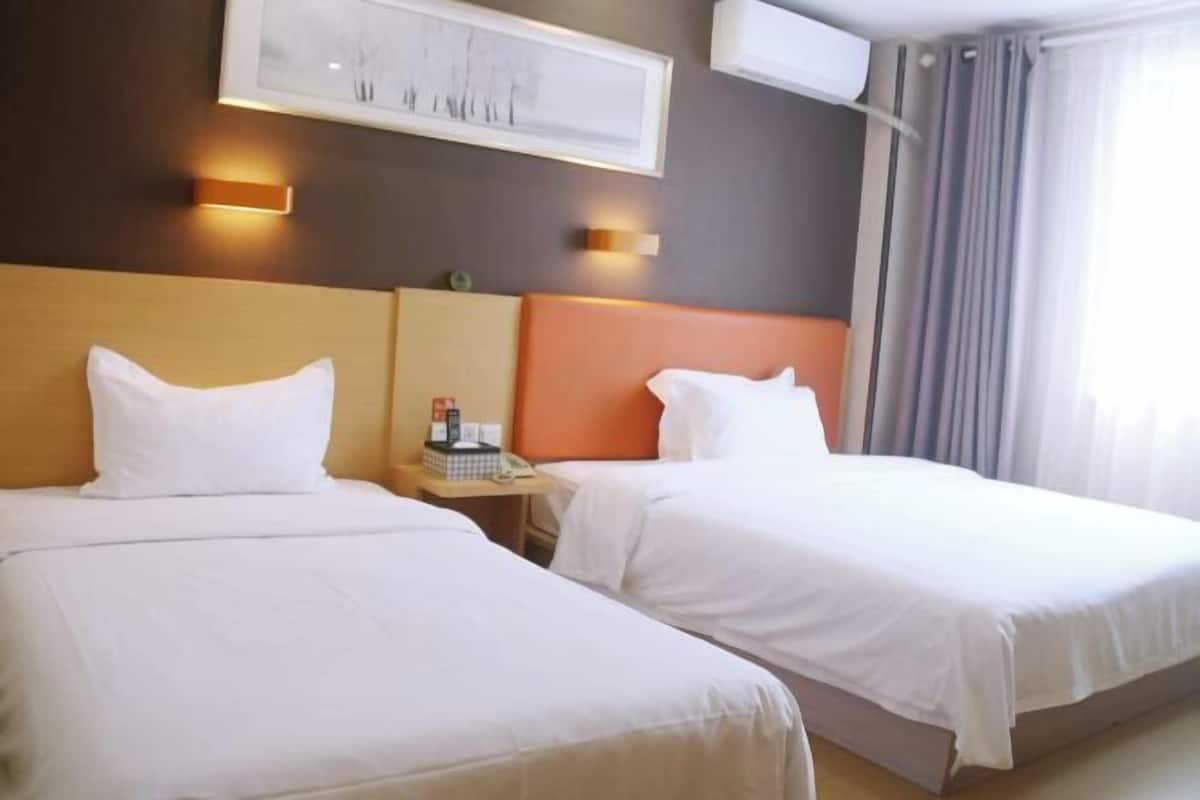 A hotel room with two beds, a framed picture on the wall, and a nightstand with a phone and a bottle.