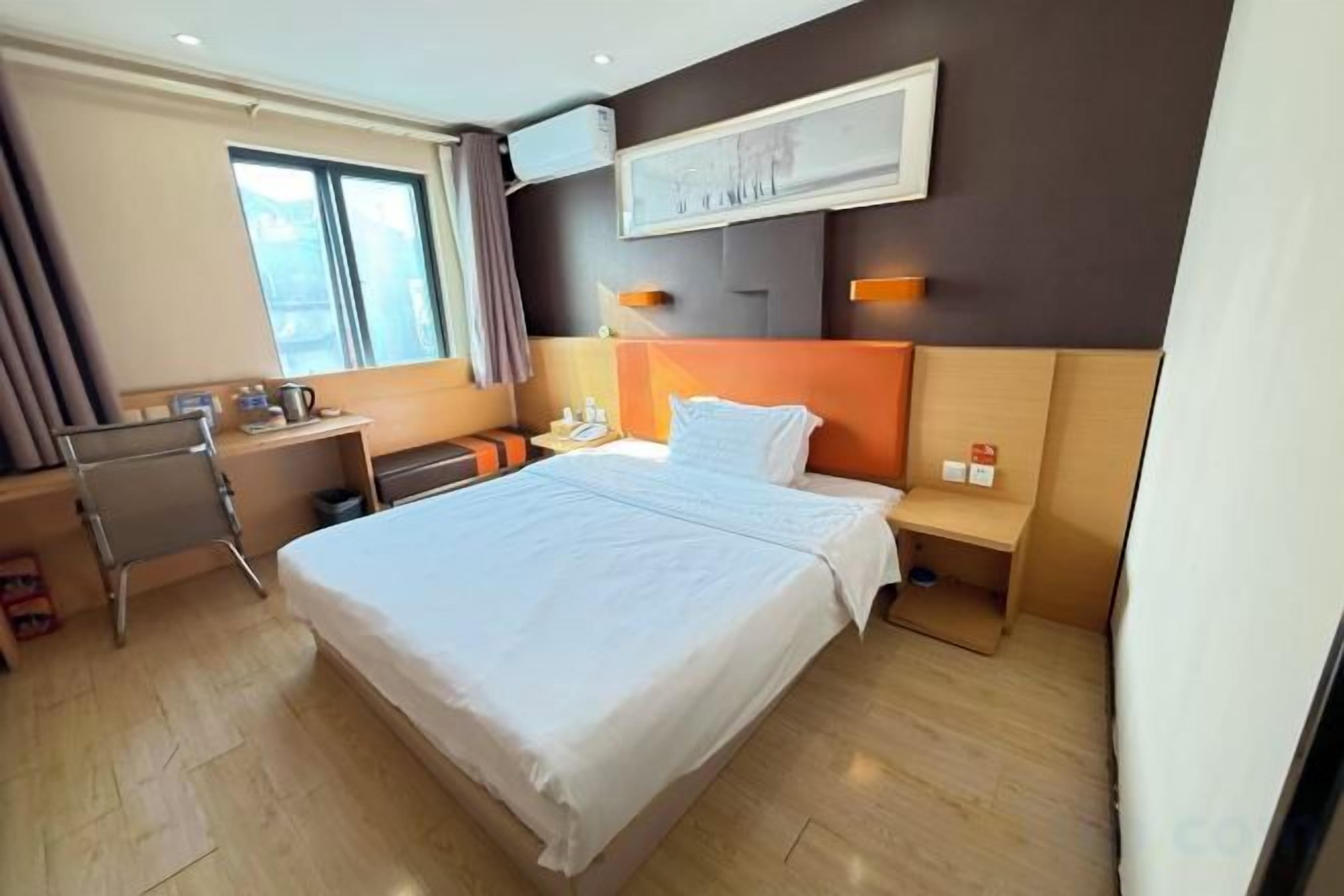 A hotel room with a large bed, a desk, a chair, and a bedside table.