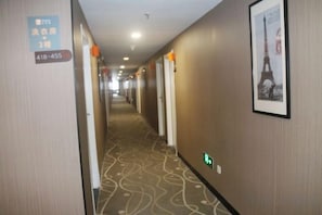 Un corridoio d'hotel con una moquette a motivi, porte e un quadro con la Torre Eiffel.