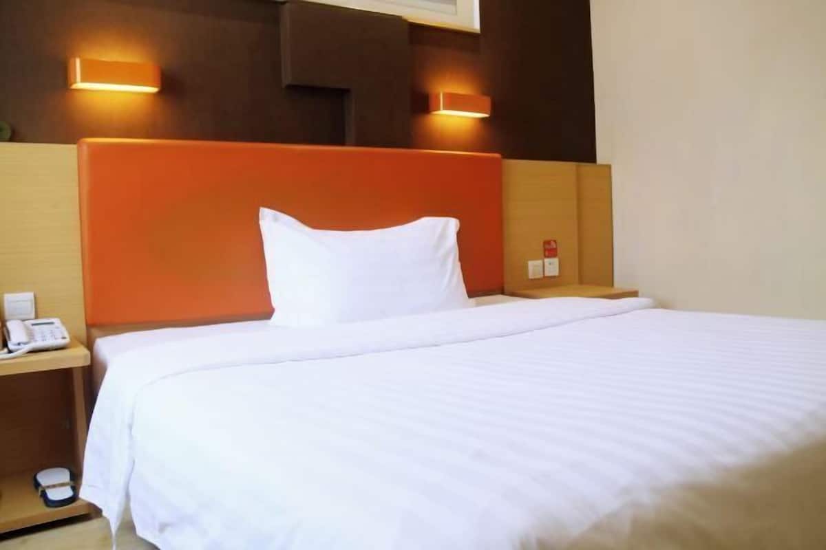 A hotel room with a large bed, two bedside tables, and a headboard with integrated lighting.