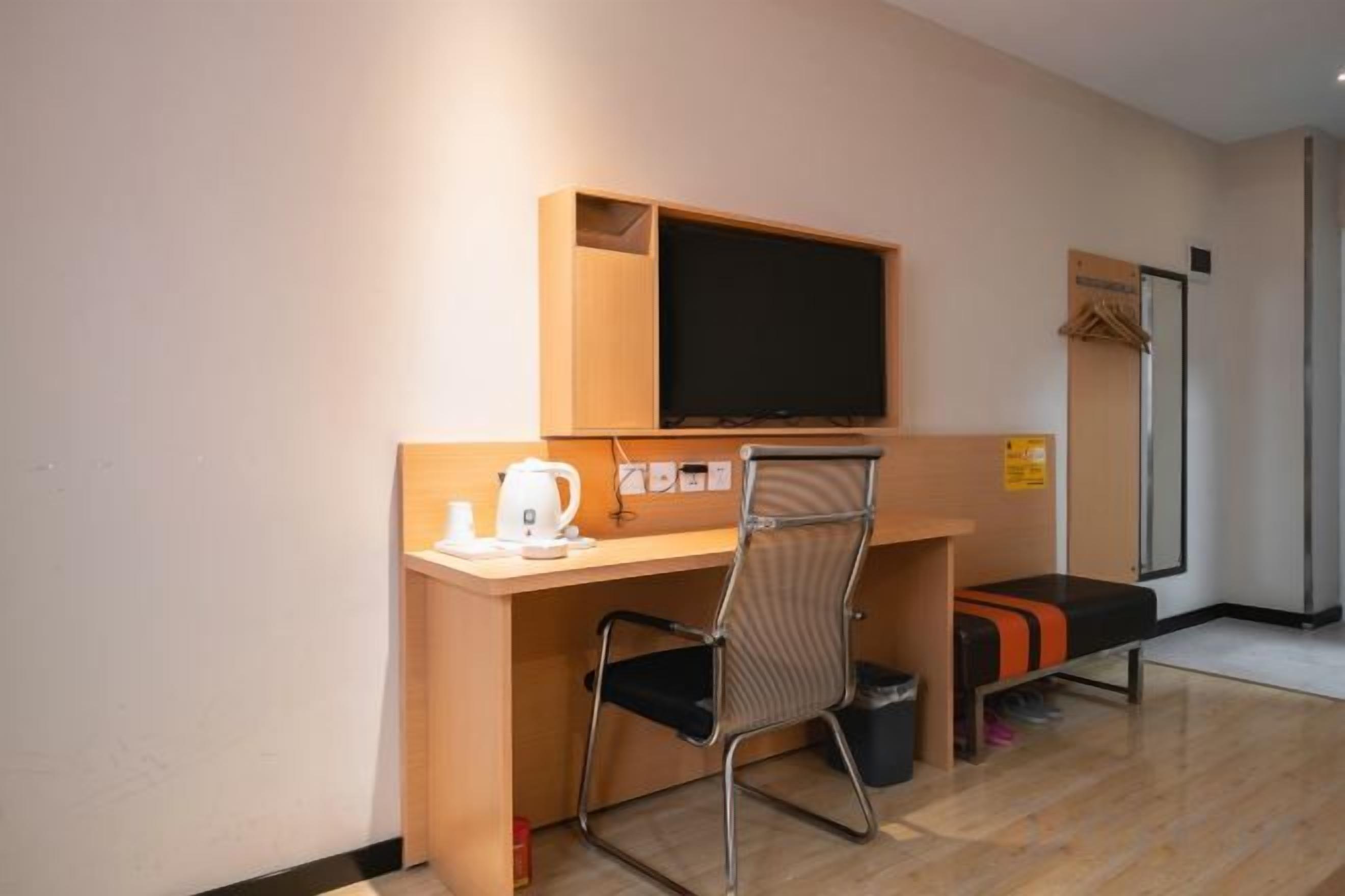 Una habitación compacta con un escritorio de madera, una silla, un televisor y un pequeño banco.