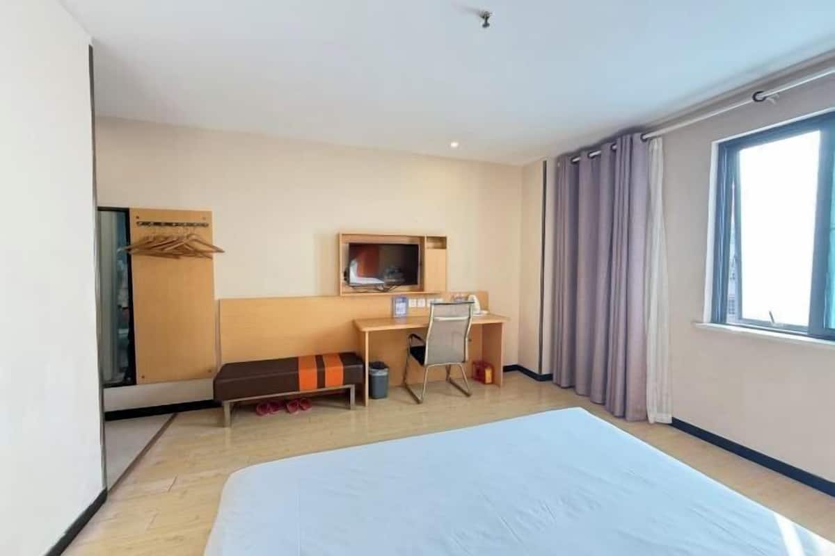 A hotel room with a large bed, a desk with a chair, a television, and a wardrobe.