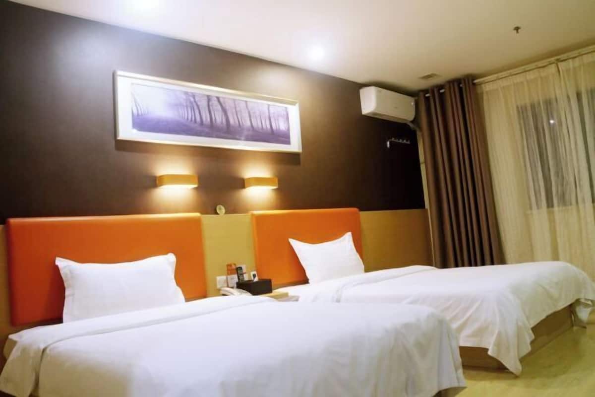A hotel room with two beds, a large framed picture on the wall, and a window with curtains.