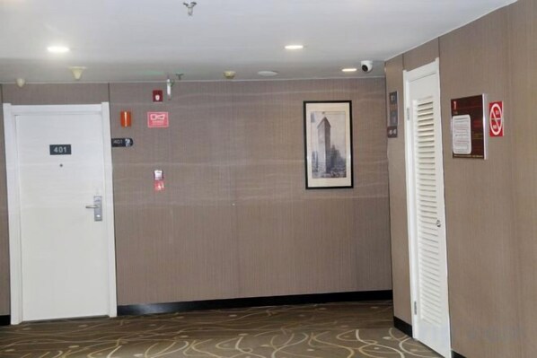 A hotel corridor with a closed door marked '401', a fire alarm, a framed picture on the wall, and a no-smoking sign. - Xinyuan Hotel (Xiamen Airport Dianqian) (Xiamen)