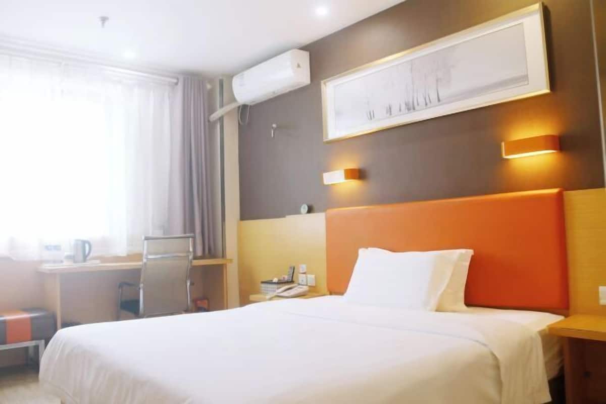 A hotel room with a bed, a desk, a chair, a telephone, and a wall-mounted air conditioner.