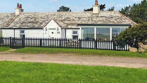 Ein weißes Cottage mit einem Steinziegeldach, einem schwarzen Lattenzaun und einem grünen Rasen.