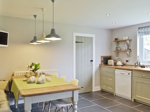 A kitchen with a dining table, chairs, a radiator, a dishwasher, and a window with blinds. - 2 bedroom accommodation in Southerness near Dumfries (Southerness near Dumfries)