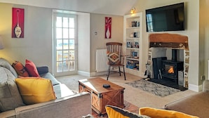 Ein Wohnzimmer mit einer Couch, Sesseln, einem Kamin, einem Bücherregal und einem Fernseher.