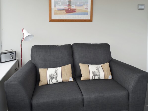 A grey sofa with two decorative pillows, a framed picture above, and a lamp on a white table. - 2 bedroom accommodation in Southerness near Dumfries (Southerness near Dumfries)