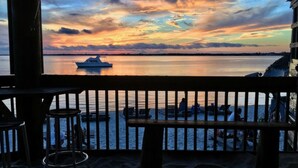 A sunset view from a balcony overlooking a calm sea with a boat and people on the shore. - Beachview 111, Navarre Beach (Navarre)