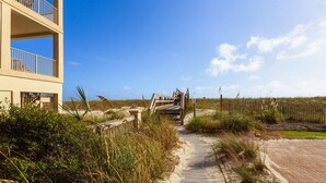 A pathway leading to a beach area with a wooden gate, a building with balconies, and a clear sky. - Beachview 111, Navarre Beach (Navarre)