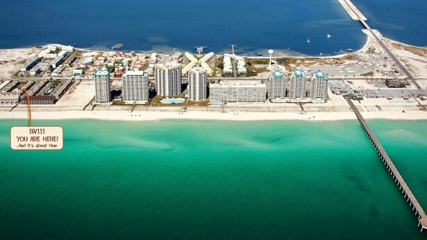An aerial view of a coastal area with a long pier extending into the sea, surrounded by high-rise buildings and a sandy beach. - Beachview 111, Navarre Beach (Navarre)