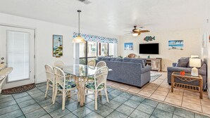 A living room with a dining area, a gray sofa, a TV, and a ceiling fan. - Beachview 111, Navarre Beach (Navarre)