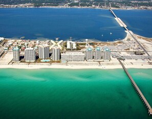 Eine Luftaufnahme einer Küstenregion mit einer langen Mole, die sich ins Meer erstreckt, umgeben von Hochhäusern und einem Sandstrand.