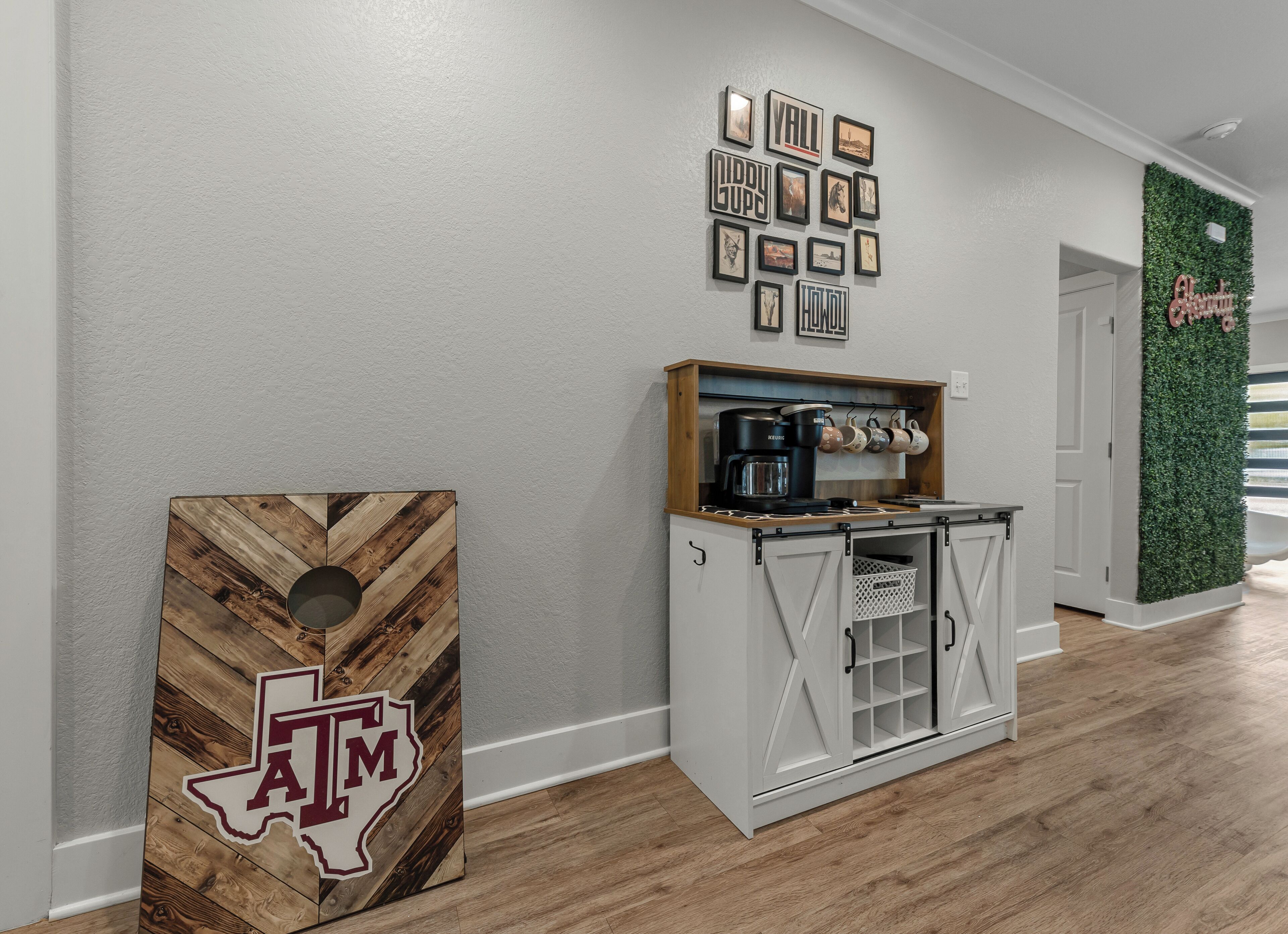 Un couloir avec un mur blanc, un drapeau du Texas en guise de décoration, un coin café et un mur vert agrémenté d’un élément décoratif.