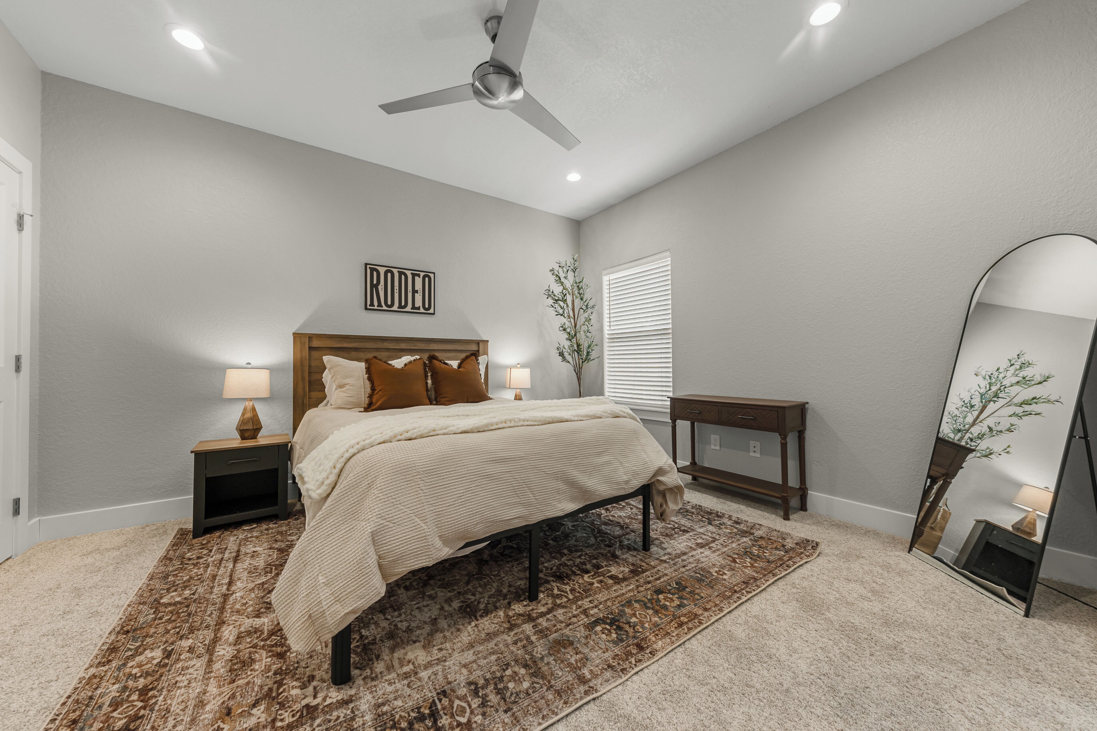 A bedroom with a bed, nightstands, a ceiling fan, a mirror, and a wall-mounted sign.