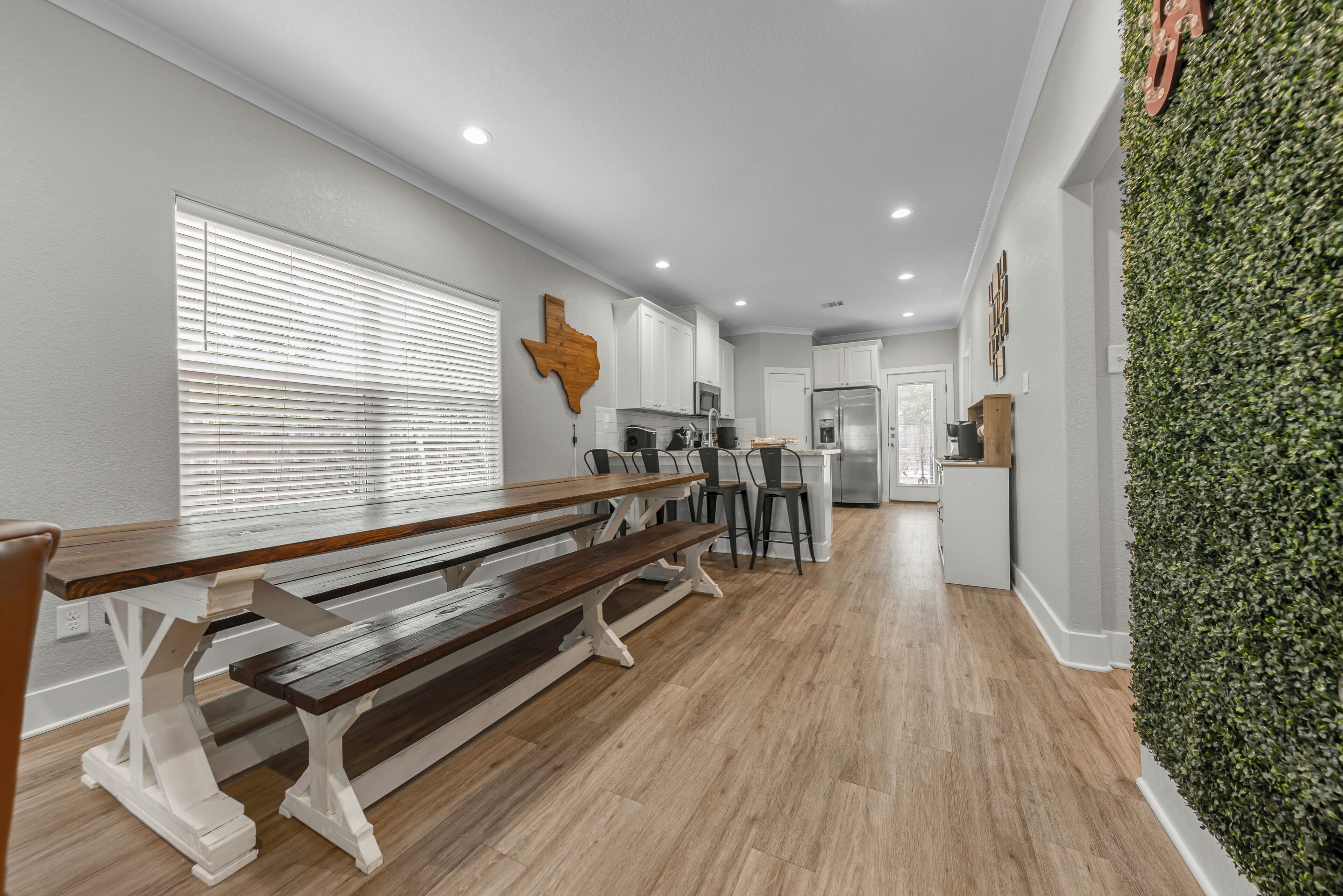 A spacious kitchen with white cabinets, a wooden bench, and a Texas-shaped wall decoration.