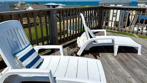 Une terrasse en bois avec deux chaises longues blanches et un coussin à rayures bleues.