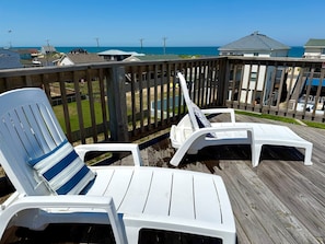 A wooden deck with two white lounge chairs and a blue-striped cushion.