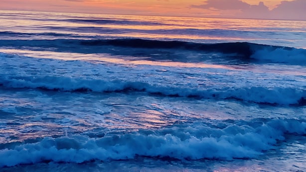 Un coucher de soleil sur l’océan, avec des vagues.