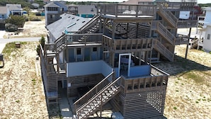 Une structure en bois à plusieurs niveaux, dotée de balcons et d’escaliers, située sur une zone sablonneuse.