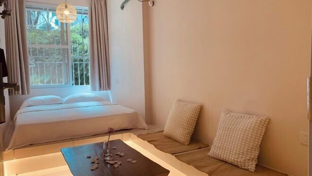 A bedroom with a bed, a bedside table with a lamp, and a window with curtains. - Xinxin Youth Hostel (Shenzhen Window of the World) (Shenzhen)
