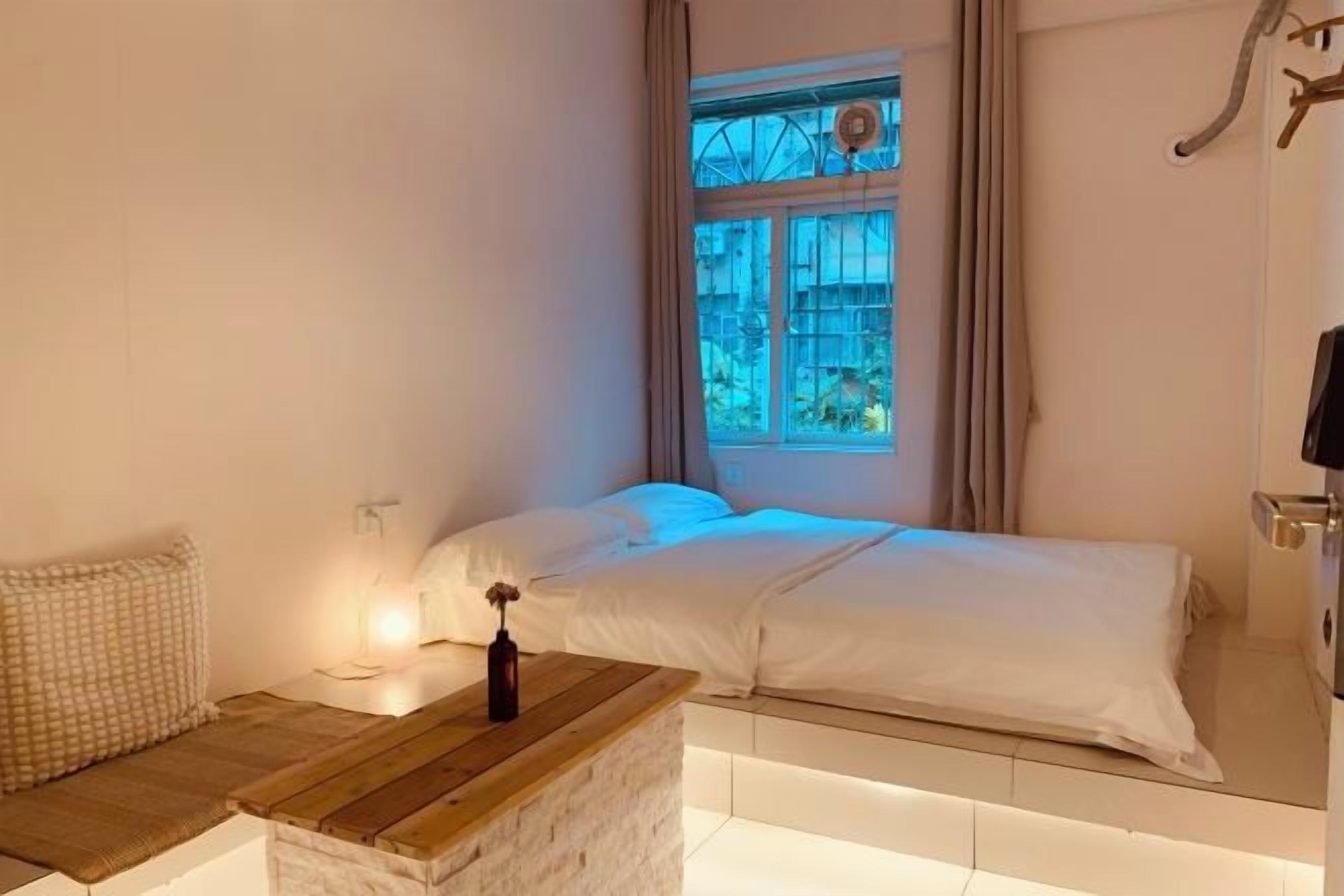 A bedroom with a bed, a bedside table with a lamp, and a window with curtains.