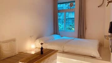 A bedroom with a bed, a bedside table with a lamp, and a window with curtains.