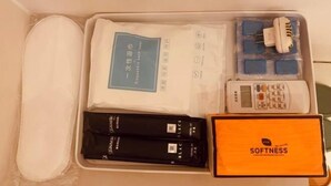 A traveler's suitcase with a white interior, containing a black and white electronic device, a blue and white power adapter, a white charging cable, and a black and white box labeled "SOFTNESS". - Xinxin Youth Hostel (Shenzhen Window of the World) (Shenzhen)
