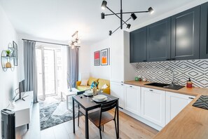 Eine moderne Küche mit weißen Schränken, einer Holz Arbeitsplatte und einer schwarzen Rückwand. Es gibt einen Essbereich mit Tisch und Stühlen, und eine Couch im Hintergrund.