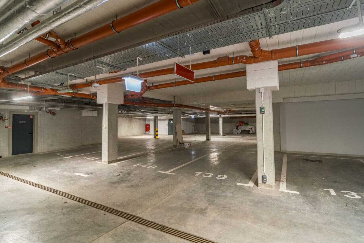 An empty parking garage with concrete floors, numbered parking spaces, and exposed ductwork.