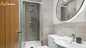 Ein modernes Badezimmer mit einer gläsernen Duschkabine, einer weißen Toilette und einem großen Waschbecken mit Spiegel darüber.