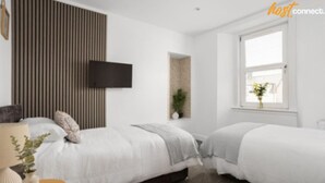 Ein modernes Hotelzimmer mit zwei Betten, einem Flachbildfernseher, einem kleinen Fenster mit Blick und einer Zimmerpflanze.