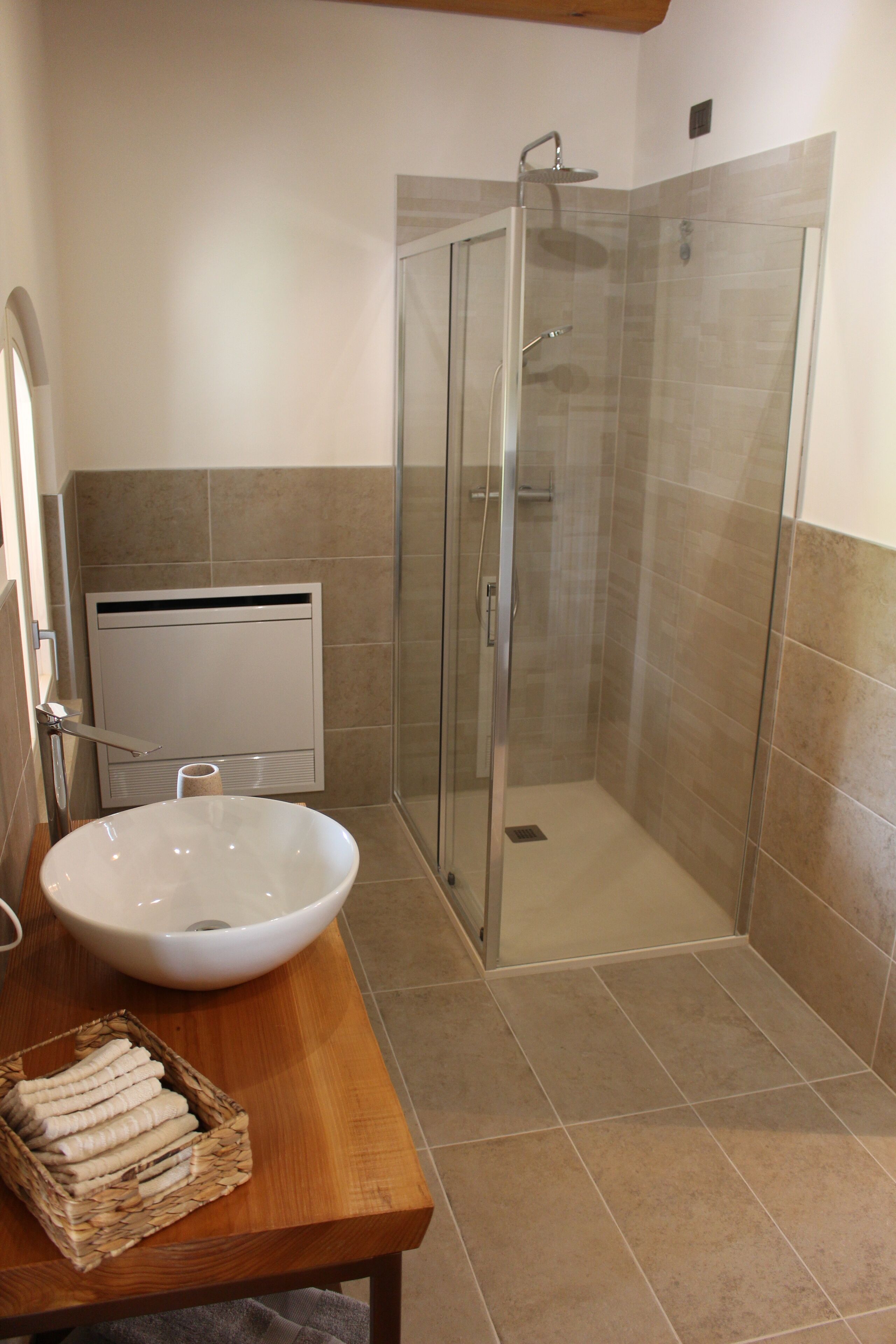 Ein Badezimmer mit weißem Waschbecken, einer Duschkabine aus Glas und einem Holztisch mit einer Korbablage für Handtücher.