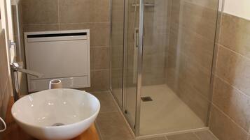 Ein Badezimmer mit weißem Waschbecken, einer Duschkabine aus Glas und einem Holztisch mit einer Korbablage für Handtücher.