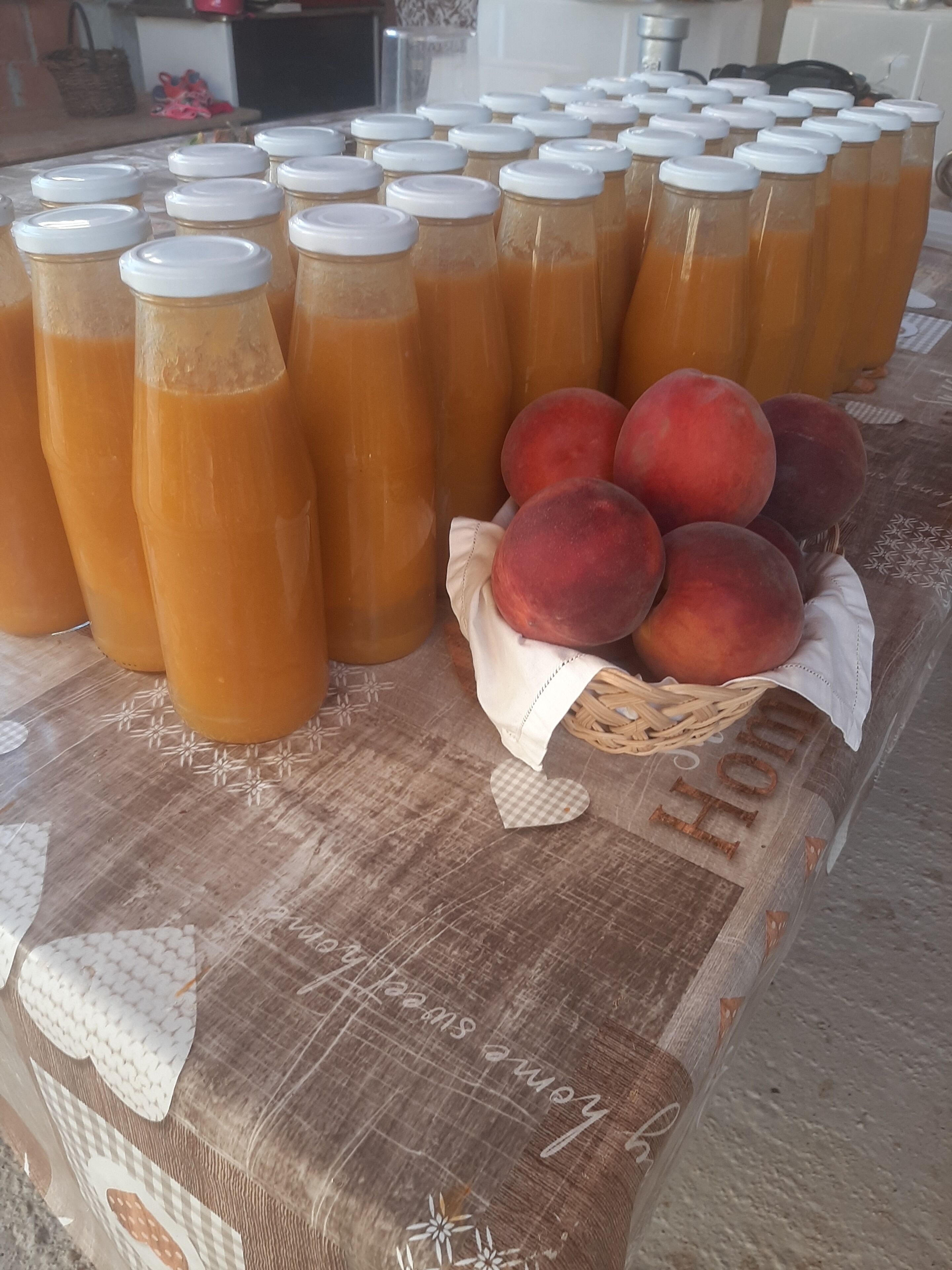 A table with multiple bottles of a beverage and a basket of peaches.
