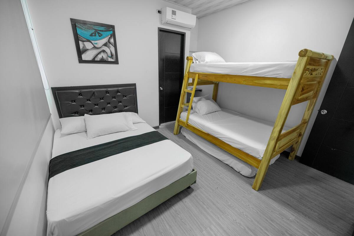 A room with a bunk bed, a single bed, a headboard, a wall-mounted air conditioner, a door, and a framed picture.