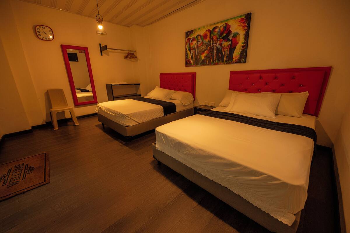 A hotel room with two beds, a large mirror, a clock, and a painting on the wall.