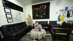 A living room with a black leather sofa, a round coffee table with a floral tablecloth, a Christmas tree, and a painting of a horse. - Hotel Puerta del Sol de Uraba (Apartadó)