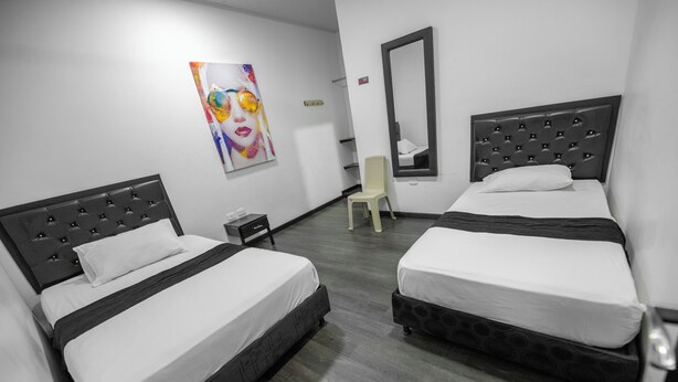A hotel room with two beds, a chair, a painting, and a mirror. - Hotel Puerta del Sol de Uraba (Apartadó)