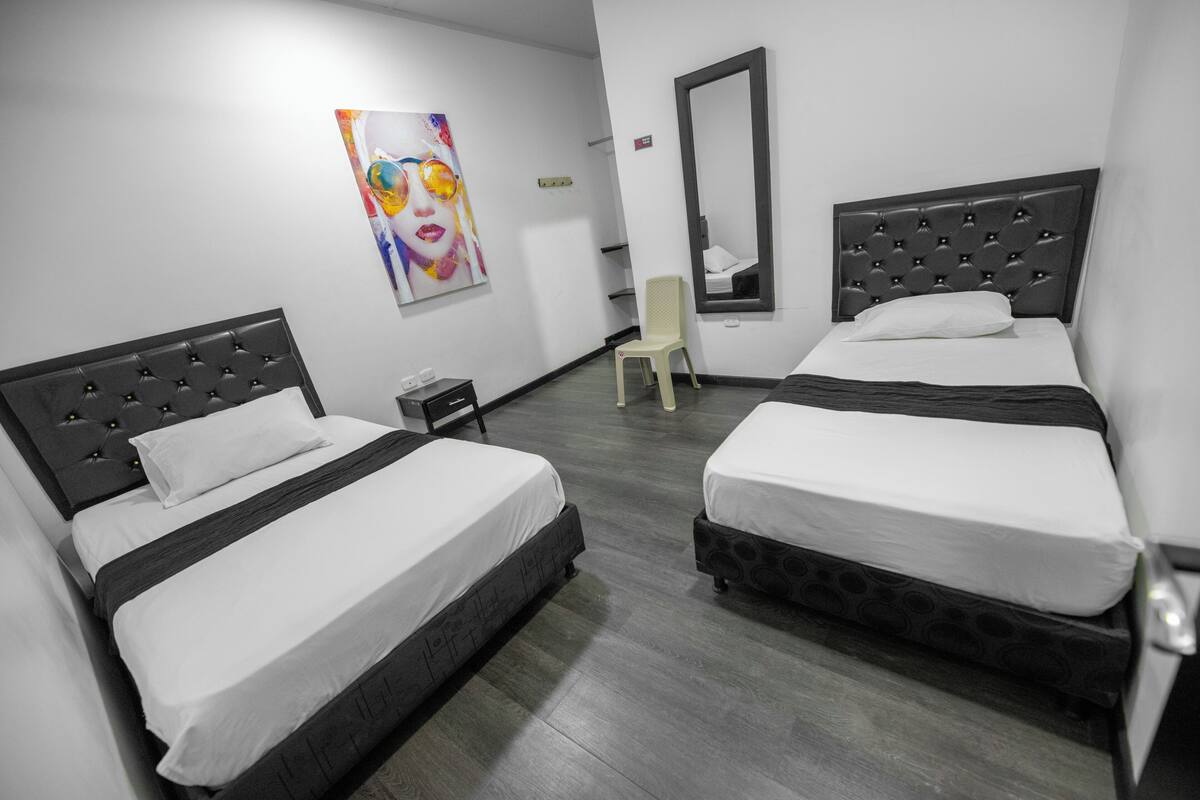 A hotel room with two beds, a chair, a painting, and a mirror.