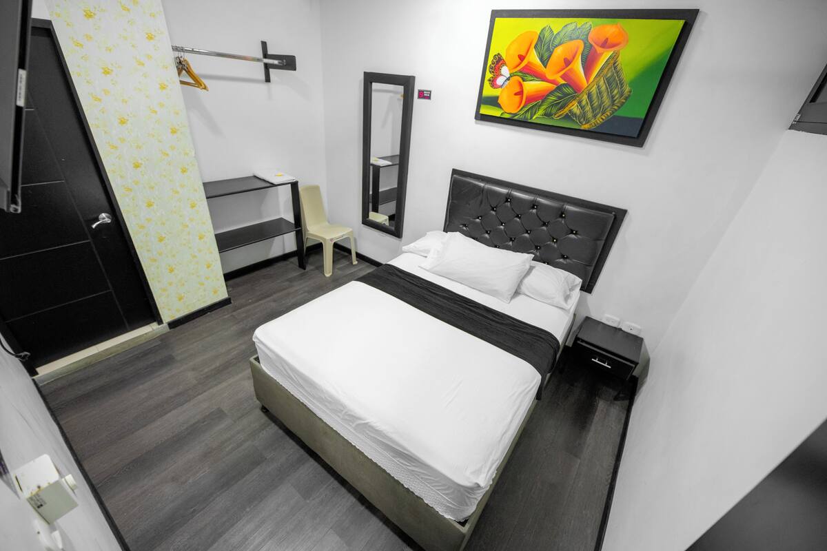 A modern hotel room with a large bed, a desk, a chair, a wardrobe, and a mirror.