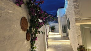A narrow alleyway with white walls, a wooden door, and a plant with purple flowers. - Montesanto 60 Suite & Relax Alberobello (Alberobello)