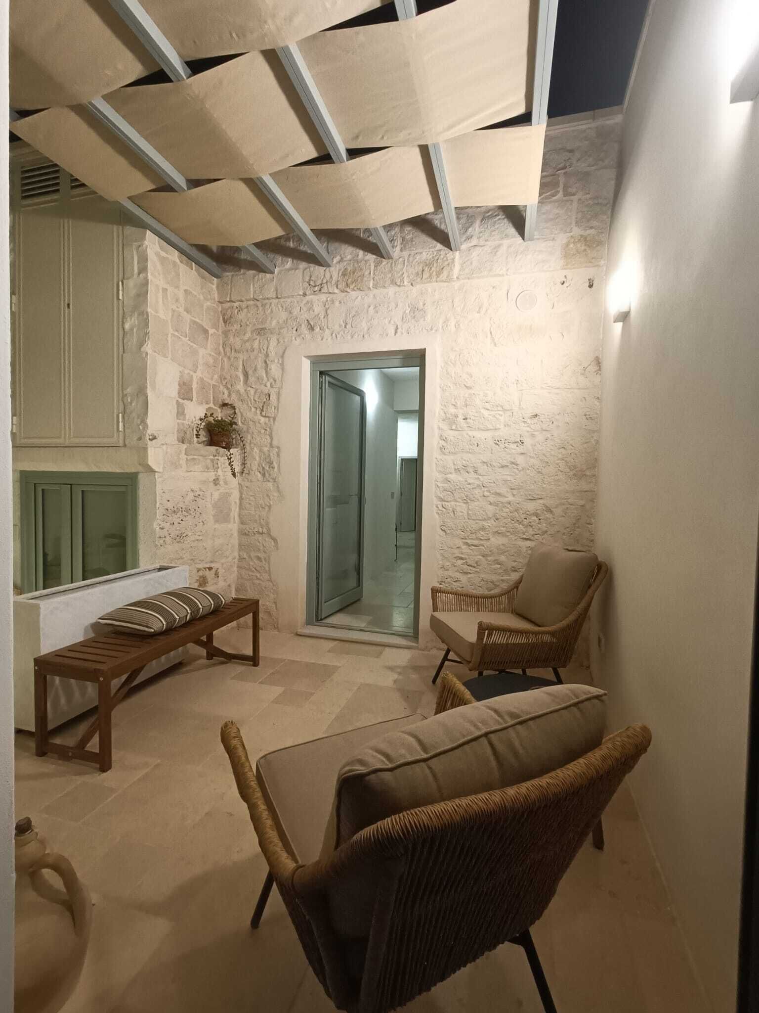 Un espace extérieur accueillant, avec un mur en pierre, un banc en bois et des chaises en osier.