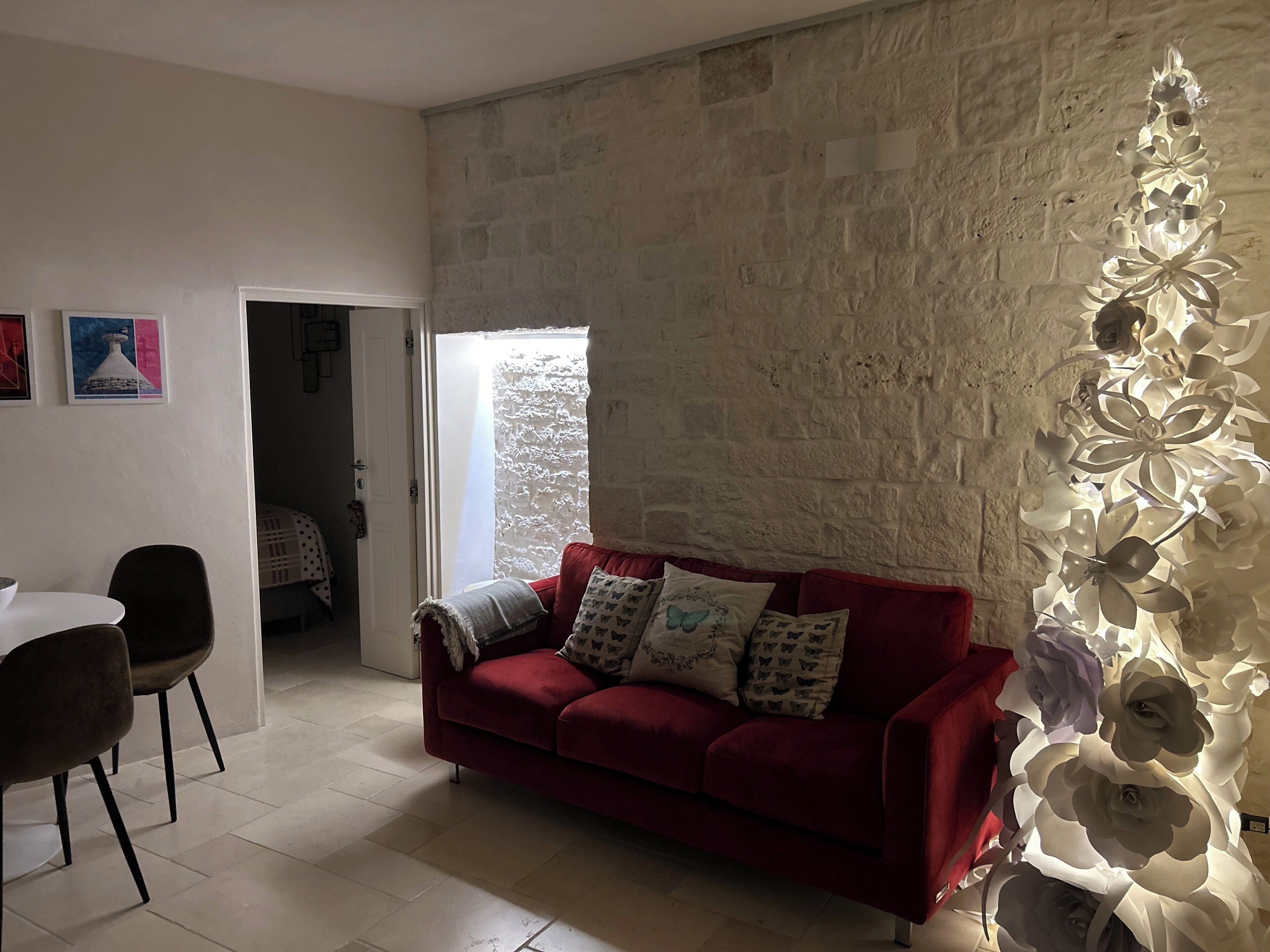 A living room with a red sofa, a white wall with a textured pattern, a door leading to another room, and a decorative light fixture.
