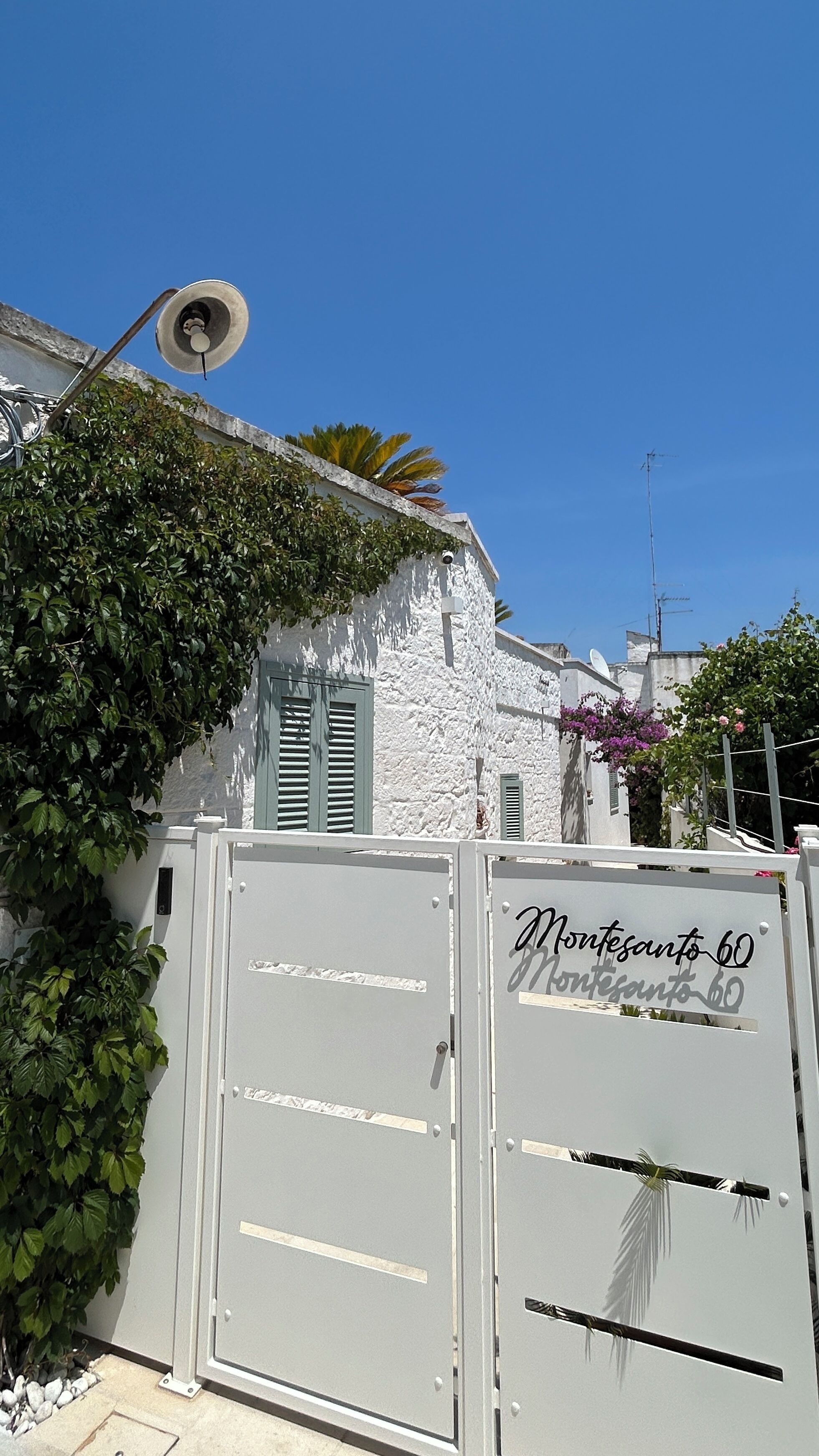 A white building with a metal gate labeled 'Monterosanto 60' and a street lamp.